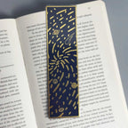 Navy blue bookmark with gold foil planets and stars, placed in open book