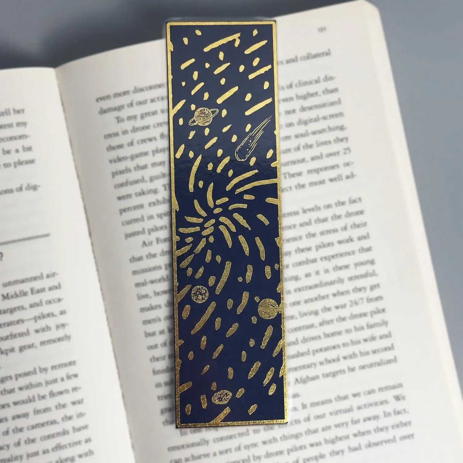 Navy blue bookmark with gold foil planets and stars, placed in open book