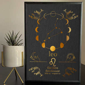 A framed artwork featuring the Leo zodiac sign with a foil finish, displayed on a table with a plant and decorative items.